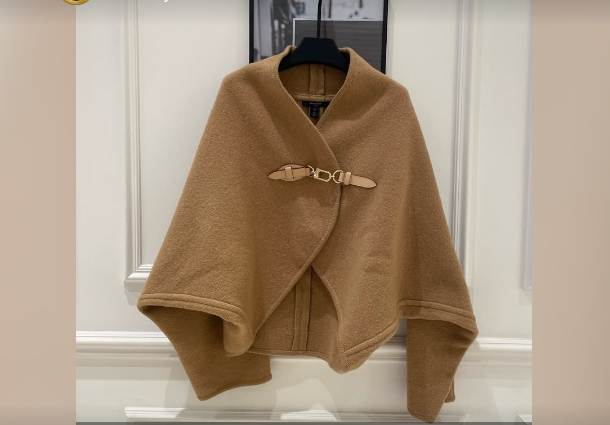 Camel wool cape poncho with leather buckle closure displayed on a hanger